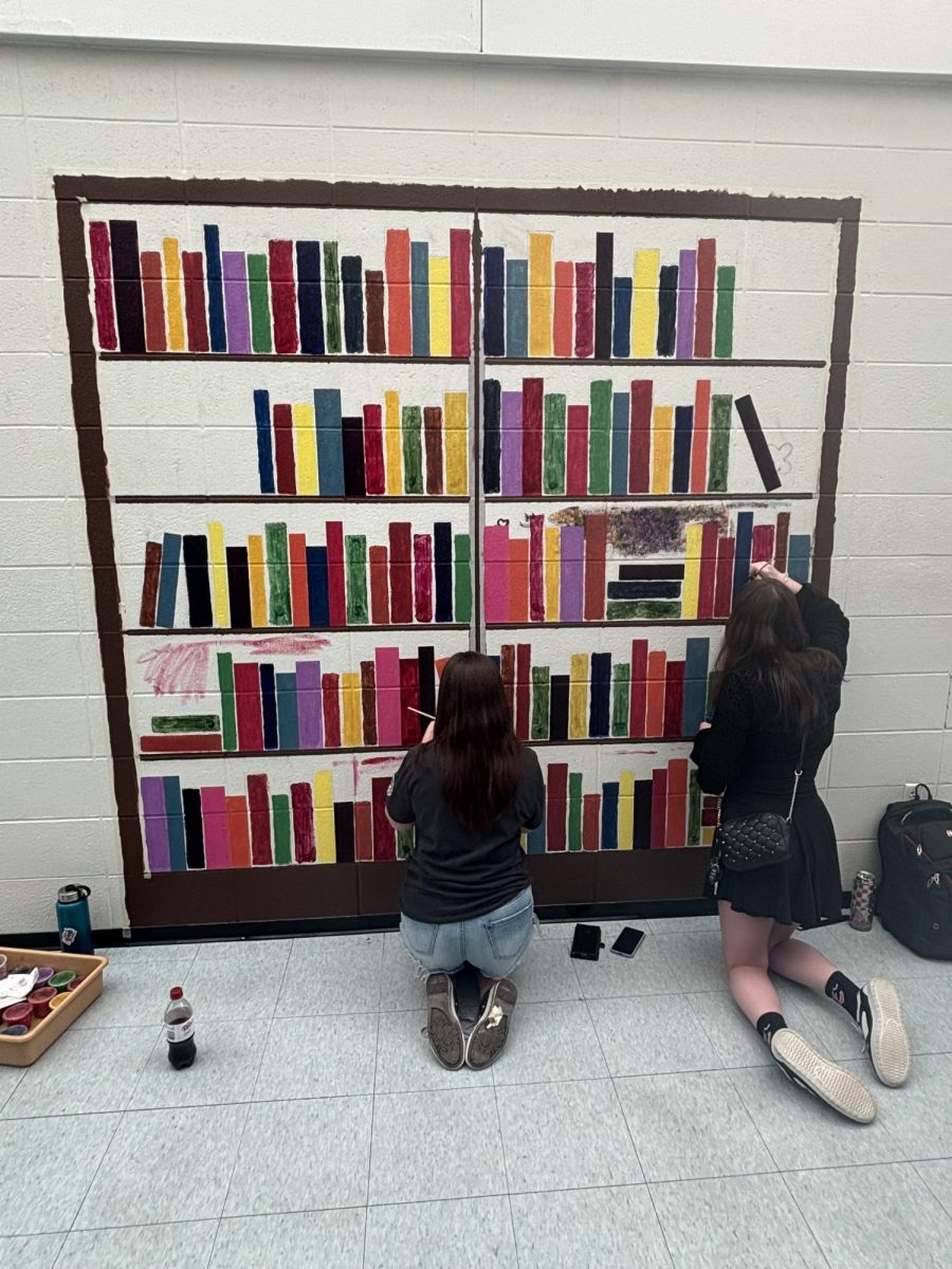 Students paint a bookshelf mural in the English hallway, adding bright colors and book covers. They started the project after getting permission from the art teacher and the principal.

